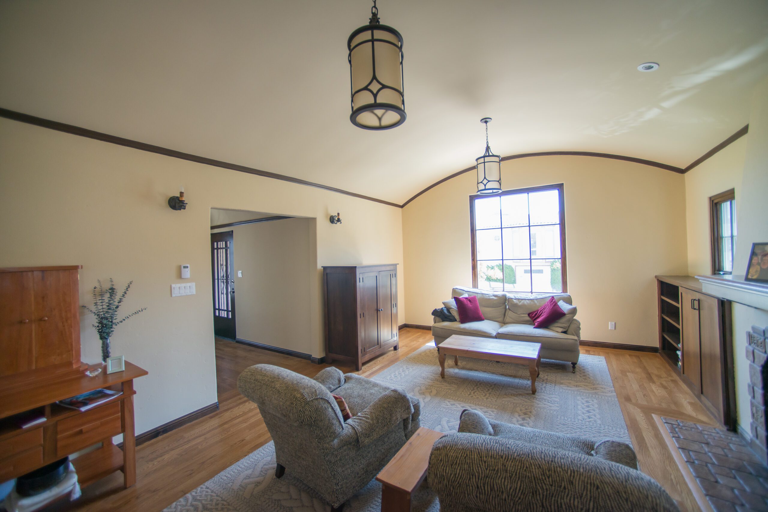 Spacious living room with vaulted ceilings, large windows, and a combination of tile and hardwood flooring.