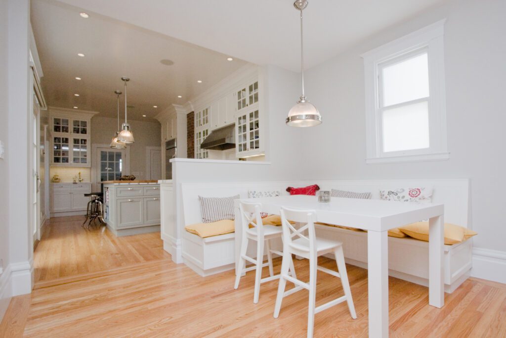 Bright and spacious kitchen interior with white cabinetry, hardwood floors, and a dining nook with bench seating.