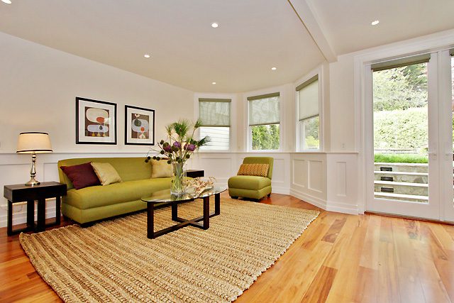 Bright living room with hardwood floors, green sofa, and multiple windows.