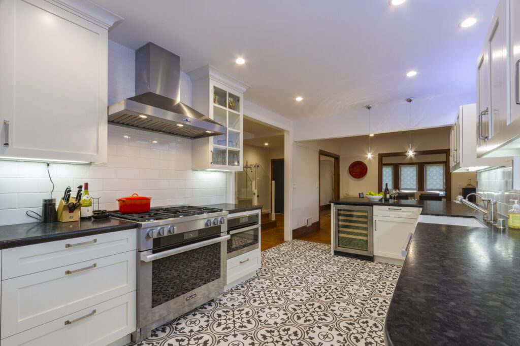 Modern kitchen interior with patterned flooring, stainless steel appliances, and white cabinetry.