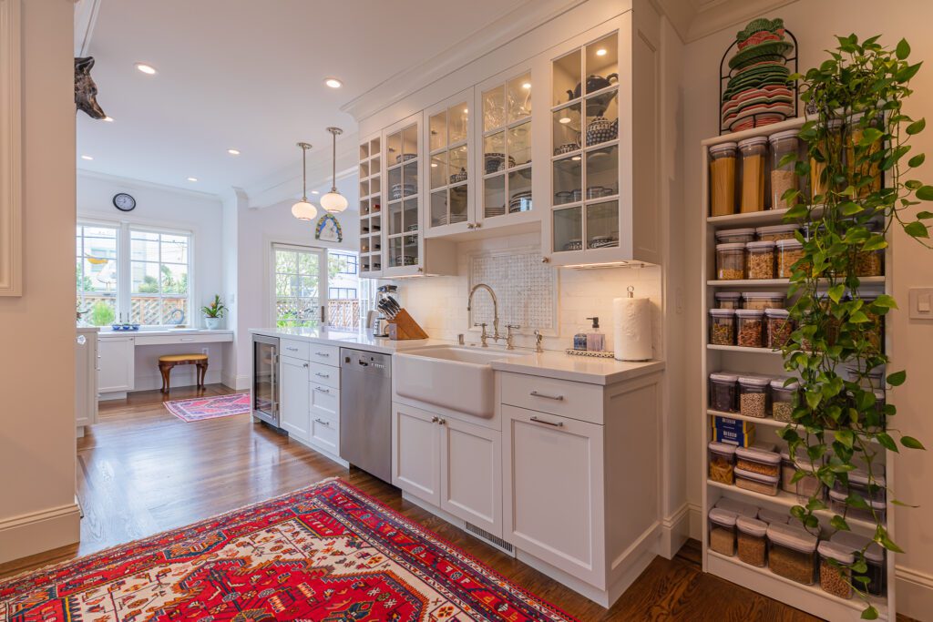 Bright kitchen interior with white cabinetry, wooden floors, and a well-organized open shelving unit.