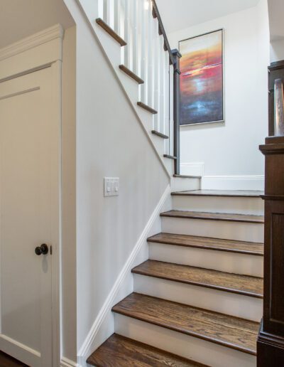 Interior of a home featuring a wooden staircase with white risers, a closed door to the left, and a wall-mounted piece of art above the staircase.
