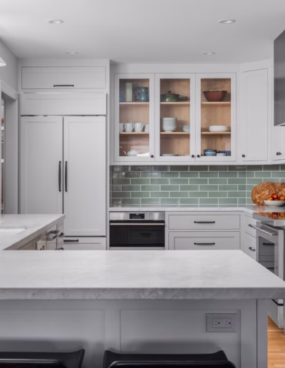 Modern kitchen with white cabinets, green subway tile backsplash, stainless steel appliances, marble countertops, and potted plants on the counters.
