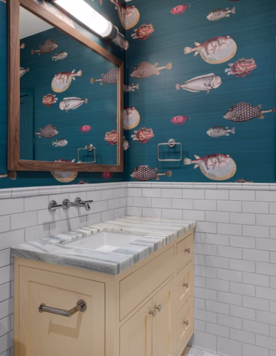 A bathroom with a yellow vanity, marble countertop, white subway tile walls, and blue wallpaper featuring various fish illustrations.